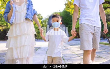 Buona famiglia che indossa la maschera medica e cammina nel parco. Foto Stock