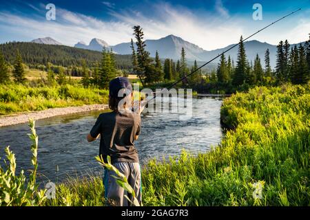 Un bambino gettando la sua canna da pesca nel fiume Crossest con uno sfondo di montagna rocciosa nel sud del Canada Alberta. Foto Stock
