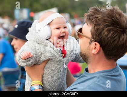 Lulworth, Dorset, Regno Unito, venerdì 30 luglio 2021 UN bambino che indossa le protezioni dell'orecchio è tenuto da suo padre il giorno 1 di Camp Bestival, Castello di Lulworth, Dorset. Credit: DavidJensen / Empics Entertainment / Alamy Live News Foto Stock