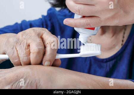 Asian anziana donna che prova ad usare spazzolino da denti, tremore della mano. Salute dentale Foto Stock