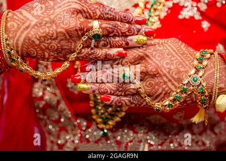 Tradizionali gioielli nuziale e decorazione henné sulle mani della sposa durante una cerimonia religiosa a nozze indù Foto Stock