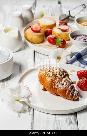 Appetitosi croissant croccanti e frittelle al formaggio di Cottage con fragole fresche e marmellata di frutti di bosco. Colazione deliziosa e sana. Cibo dolce. Woo Foto Stock