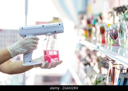 primo piano della mano del personale che indossa i guanti utilizzando il pulitore disinfettante spray portatile per sanitari usb nano per il cuvid19 in negozio Foto Stock