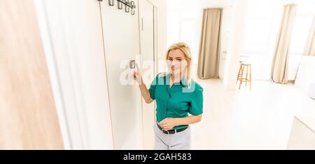 donna che regola la temperatura di riscaldamento con un moderno termostato wireless installato sulla parete bianca a casa. Concetto intelligente di regolazione del riscaldamento domestico Foto Stock