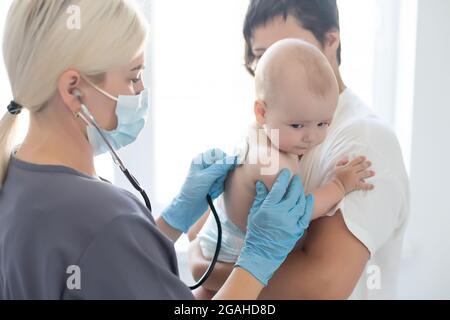 Femmina medico che esamina la bambina piccola sorridente, tenuta dalla madre Foto Stock