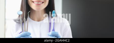 Sorridente dentista femmina che tiene in mano lo strumento e lo spazzolino da denti Foto Stock