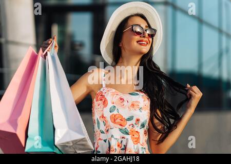 Giovane allegro fashionista a piedi lungo la strada, shopping con acquisti in città sullo sfondo di vetrine di un centro commerciale, sh Foto Stock