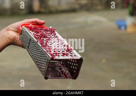 grattugia in acciaio inox con pezzi di barbabietola rossa tenuti in mano. Grattugia per la triturazione delle verdure Foto Stock