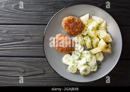 I Kotlety Mielone sono polpettine di carne fritta in padella tradizionale polacca serviti con patate bollite e insalata di cetrioli nel piatto sul tavolo. Horizo Foto Stock