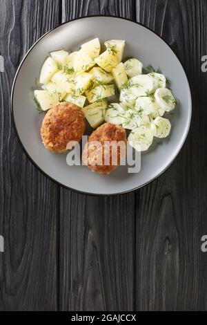 Kotlety Mielone Ricetta tradizionale polacca di maiale macinato con patate bollite e insalata di cetrioli nel piatto sul tavolo. Verticale superiore Foto Stock