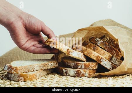 Mano dell'uomo che raccoglie una fetta di pane di pasta acida dall'interno di un sacchetto di carta Foto Stock