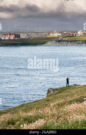 La figura di un turista che si trova a Penire Point East guardando indietro a Fistral Beach attraverso la Fistral Bay a Newquay in Cornovaglia. Foto Stock