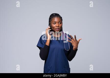 Sorridente dottoressa afroamericana isolata su sfondo bianco. Dottore femminile in abito medico bianco che parla sul telefono cellulare. Personale sanitario Foto Stock