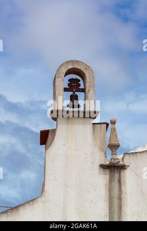 Dettaglio del piccolo campanile e pinnacolo in cima alla cappella cristiana portoghese contro il cielo blu nuvoloso Foto Stock