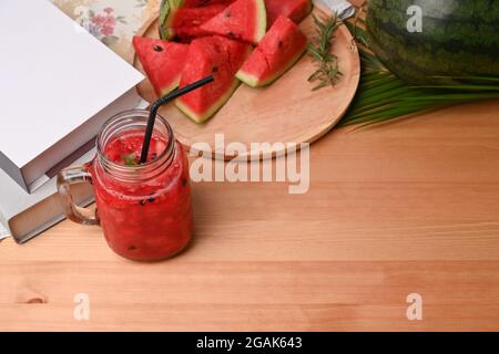 Frullato fresco in vaso di vetro con fette di anguria su sfondo di legno. Foto Stock