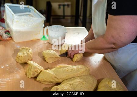 Mujer caucásica masando masa para hacer pan y bizcochos en una mesa color madera con luz de día, en una panadería. Foto Stock