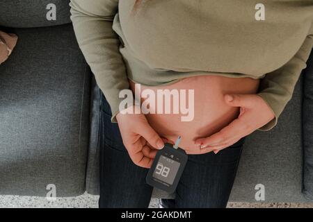 Colpo di testa di una donna incinta che tiene un glucometro con il risultato Foto Stock