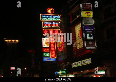 Segnaletica stradale al neon di notte a Bangkok utilizzando lettere romane, caratteri cinesi e la scritta thailandese, Thailandia Foto Stock