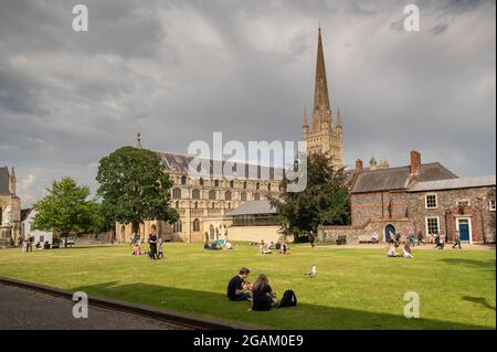 Una vista della cattedrale di Norwich e dei suoi terreni con persone sedute a mangiare e bere sull'erba Foto Stock