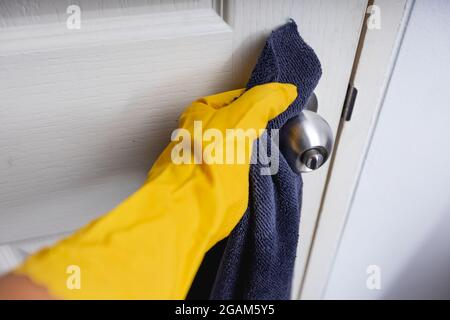 Primo piano vista a portata di mano in guanti protettivi gialli disinfezione della maniglia della porta durante la pulizia a casa, concetto di protezione coronavirus Foto Stock