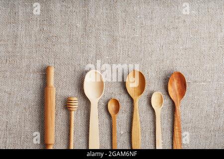 Cucchiai artigianali fatti da diversi tipi di legno giacciono in fila su un tessuto di tela di canapa Foto Stock