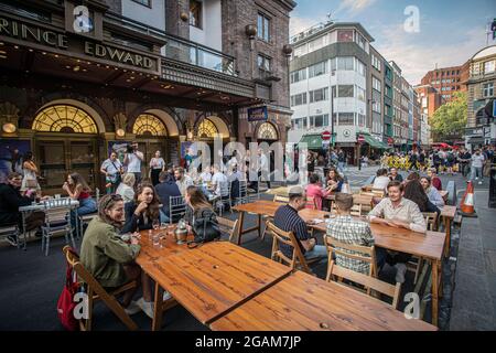 Persone che bevono sui tavoli posti fuori su Old Compton Street a Soho, Londra, Regno Unito. Foto Stock