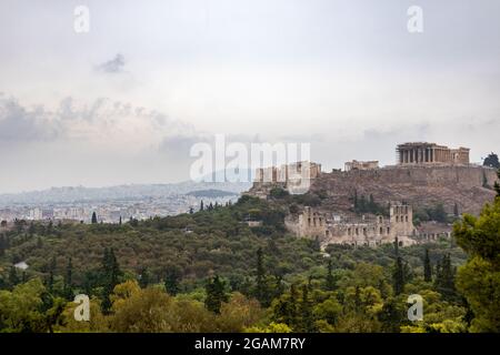 Collina dell'Acropoli (Partenone, Propylaea, Templi, Odeon di Erode Attico) e città bianca nel verde estivo. Atene antico punto di riferimento storico da Fi Foto Stock