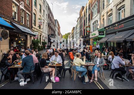 La gente mangia sui tavoli del ristorante posti all'esterno su Frith Street a Soho, Londra, Regno Unito Foto Stock