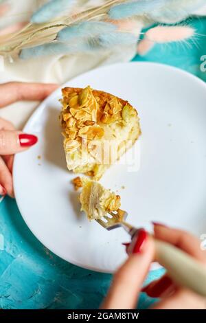 Le mani di donna irriconoscibile mangiano un pezzo di torta di mela o di pera con i dadi di caramello sul tavolo blu con luce solare, spazio di copia, vista dall'alto. Foto Stock