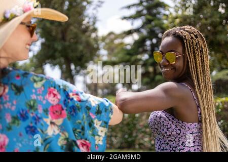 Due donne di diverse etnie in abiti estivi si inchinano in un giardino. Foto Stock