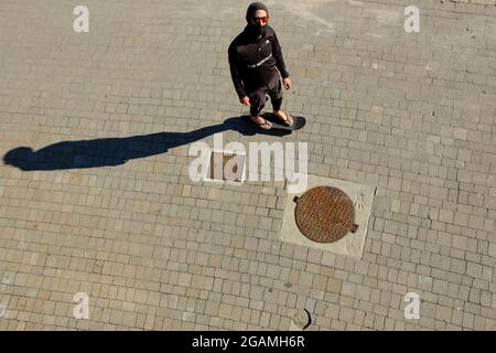 Giovane adulto che indossa occhiali da sole e una maschera che pattina su una tavola da skate, vista dall'alto. Foto Stock