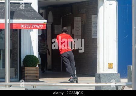 Slough, Berkshire, Regno Unito. 20 luglio 2021. Un giovane guida illegalmente un e-scooter in un'area pedonale fuori Slough High Street. Credito: Maureen McLean/Alamy Foto Stock