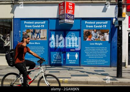 Slough, Berkshire, Regno Unito. 20 luglio 2021. Gli acquirenti passino oltre Proteggiti dalle bandiere Covid-19 in Slough High Street. Gli acquirenti a Slough oggi indossavano ancora maschere facciali, anche se non è più un requisito legale nei negozi dal sollevamento della misura di blocco Covid-19 ieri. I casi di Positive Covid-19 continuano a rischiare di mettere una forte tensione sull'NHS. Credito: Maureen McLean/Alamy Foto Stock