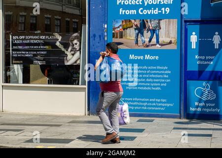 Slough, Berkshire, Regno Unito. 20 luglio 2021. Gli acquirenti passino oltre Proteggiti dalle bandiere Covid-19 in Slough High Street. Gli acquirenti a Slough oggi indossavano ancora maschere facciali, anche se non è più un requisito legale nei negozi dal sollevamento della misura di blocco Covid-19 ieri. I casi di Positive Covid-19 continuano a rischiare di mettere una forte tensione sull'NHS. Credito: Maureen McLean/Alamy Foto Stock