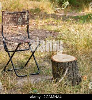 Una sedia di tourist pieghevole di tela siede vicino ad un tavolo di makeshift sotto forma di un ceppo di legno. Foto Stock