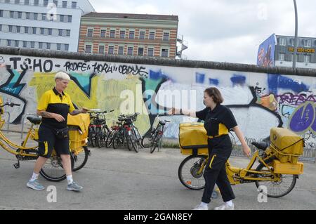 Due mail carrier femminili vicino al Muro di Berlino a Friedrichshain, Berlino, Germania - Luglio 2021. Foto Stock