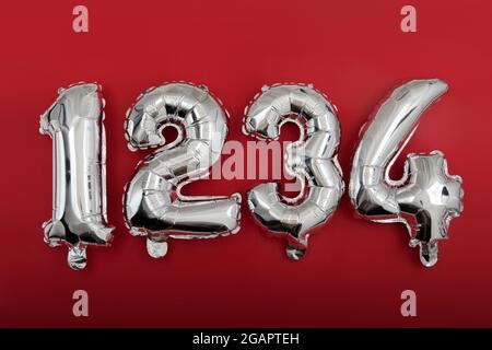 Vista dall'alto di palloncini con numero in argento lucido disposti in fila da 1 a 4 su sfondo rosso Foto Stock