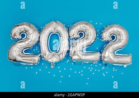 Dall'alto di palloncini in argento con 2022 anni su sfondo blu con confetti a forma di stella Foto Stock