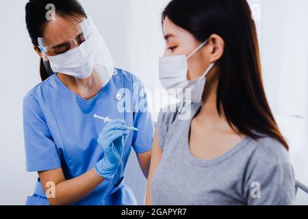 Giovane donna asiatica seduto in ufficio medico e ottenere un colpo di influenza nel suo braccio. Infermiere in maschera medica viso con siringa e dando paziente femmina m Foto Stock