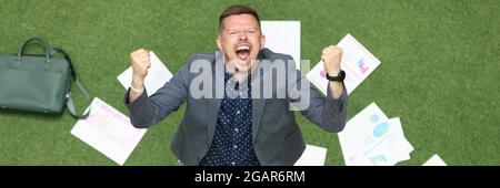 L'uomo gioioso alza le mani e grida sul pavimento giace business graphics Foto Stock