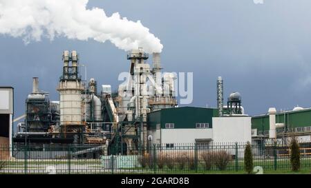 Impresa di lavorazione del legno sullo sfondo di un cielo grigio cupo. Il fumo denso proviene dal camino di fabbrica. Inquinamento atmosferico e inquinamento ambientale Foto Stock