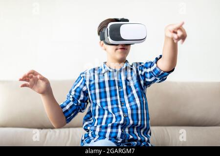 Ragazzo adolescente con occhiali VR muovendo le braccia e gesturando. Concetto di nuove tecnologie a casa. Foto Stock