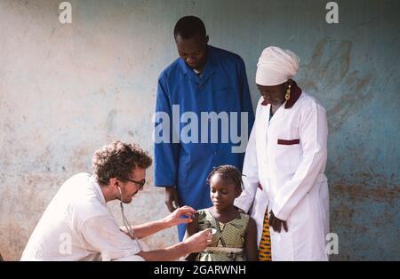In questa immagine, uno staff medico multietnico sta effettuando un esame polmonare su una timida studentessa in un ospedale dell'Africa occidentale Foto Stock