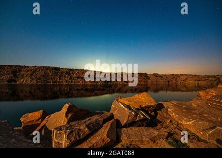 Un lago molto piccolo e bello circondato da grandi cumuli di rifiuti di pietra da duro lavoro nella miniera Foto Stock