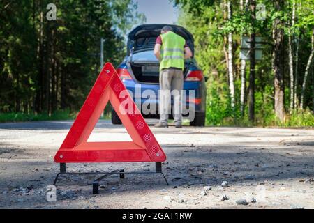Il segnale di avvertenza rosso si trova sul lato della strada accanto al veicolo danneggiato Foto Stock