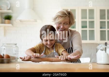 Felice nonna matura insegnando adorabile nipote a arrotolare l'impasto Foto Stock