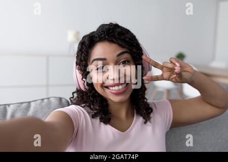 Selfie e video per blog, tecnologia moderna, positivo e felice blogger live per i social network. Sorridente giovane afroamericana in headphon wireless Foto Stock