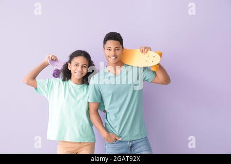 Fratello afroamericano e sorella con skateboard su sfondo a colori Foto Stock