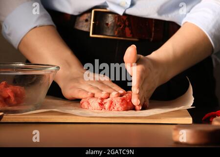 Donna che prepara gustosi cutlet fatti di forcemeat fresco su sfondo scuro, primo piano Foto Stock