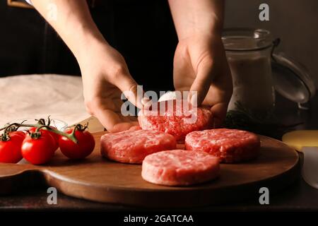 Donna che prepara gustosi cutlet fatti di forcemeat fresco su sfondo scuro Foto Stock